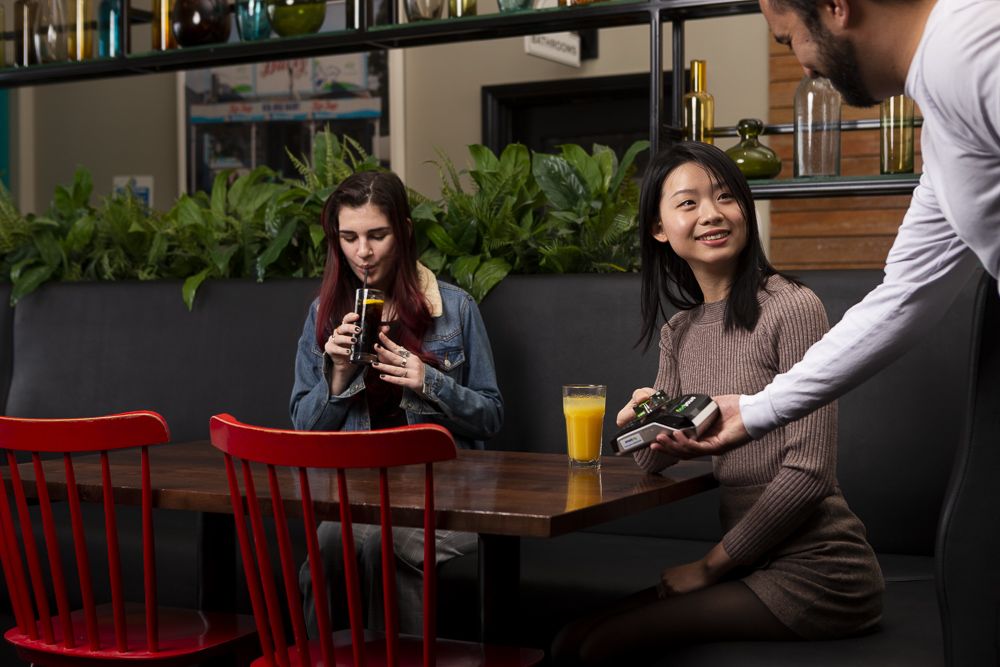 Lady at a bar paying on the payment terminal with her phone